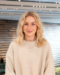 An adult with light skin, wavy blonde shoulder-length hair, and a cream jumper.