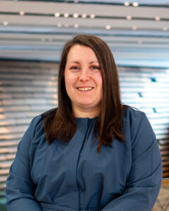 An adult with light skin, long straight dark brown hair, and a navy blue dress.