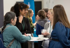 A group of adults standing at a small table and engaging in conversation.
