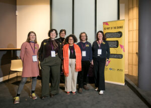 Six adults stand together smiling. Behind them a yellow pull up banner with the title 'Be part of the change'.