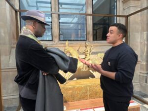 Anti-racism campaigner Lilian Thuram and Glasgow Museums Curator Nelson Cummins engage in conversation in front of a display case containing a golden figure on horseback.