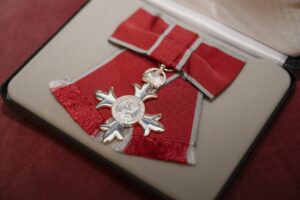 A small silver cross attached to a red ribbon with a silver trim.