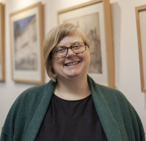 An adult with light skin, shoulder-length straight blonde hair, and tortoiseshell glasses.