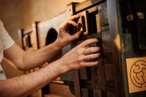 A pair of hands with light skin tone is moving sliding wooden blocks around in order to solve a puzzle.