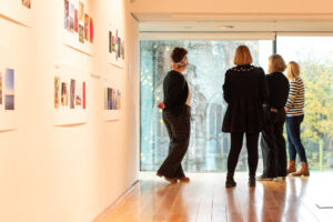Four adults stand together in a gallery and look out of a large floor-to-ceiling window.