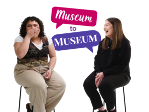 An adult with medium-light skin and curly dark brown shoulder-length hair smiles and holds their hand to their mouth. Next to them, an adult with light skin and long straight brown hair smiles and laughs. Behind them is a graphic of two speech bubbles containing the text "Museum to Museum".