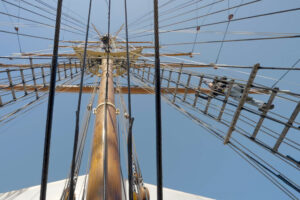 An adult ascends the rigging of a ship's mast.