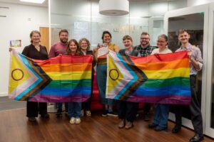 A group of adults stand together holding two pride Progress flags.