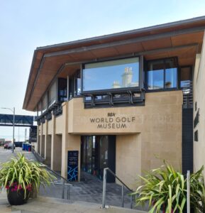 The view of the frontal approach to the R&A World Golf Museum in St Andrews, showing the stepped access. The building is made from light sandstone with a flat wooden roof.